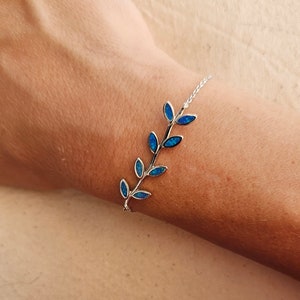 Peut inclure: Un bracelet en argent avec un motif de branche délicat orné de feuilles d'opale bleue.