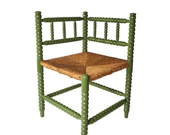 May include: A corner chair featuring a green painted wooden frame with a distinctive bobbin-style spindle design and a woven rush seat. The chair has a triangular shape with four legs and a backrest composed of two connected sections.