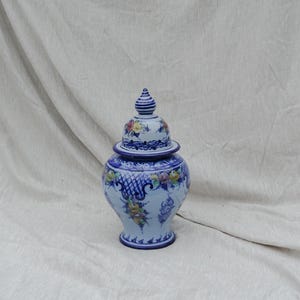 Op de afbeelding: Een blauwe en witte keramische pot met een deksel, versierd met bloemmotieven en ingewikkelde ontwerpen. De pot heeft een bolvormig lichaam en een smalle hals.
