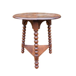 May include: A round, antique wooden table with a dark brown finish. The table has a circular top and three legs with a turned, bobbin design. The legs are connected by a triangular support.