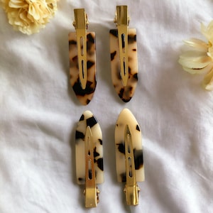 May include: Four tortoise shell hair clips with gold metal clasps. The clips are in a variety of patterns and have a brown and white color scheme.