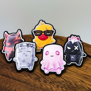 May include: A collection of five character stickers featuring a yellow duck with glasses, a black horned creature, a white pillow-shaped figure with the text Sweet Dreams, a pink ghost-like character, and a black figure in a leather jacket.