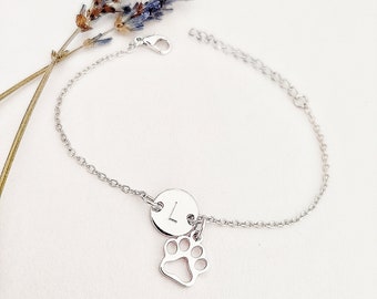 May include: A silver chain bracelet with a small silver paw print charm and a silver disc charm with the letter "L" engraved on it.