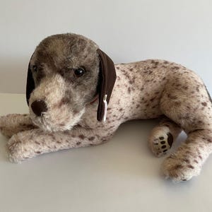 May include: A brown and white plush dog toy with brown ears and a brown nose. The dog is lying down with its paws visible.