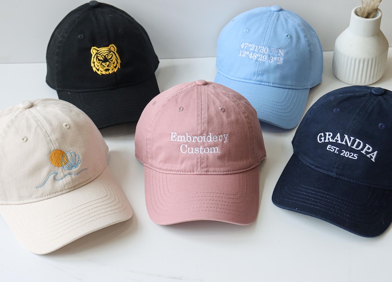 May include: Five embroidered baseball caps in different colors and designs. The caps feature a tiger, a sun and waves, the words "Embroidery Custom", coordinates, and the words "Grandpa Est. 2025".