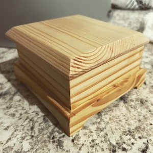 Peut inclure: Une petite boîte en bois avec un couvercle à charnière et un design simple. La boîte est en bois clair avec une finition naturelle.