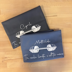 May include: Two folded t-shirts in dark gray and slate blue. Each shirt features a white graphic of a barbell with a name above it, Cyril on the gray shirt and Mathilde on the blue shirt, and the French text Ta seule limite, c'est toi-m&ecirc;me.