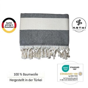 May include: A black and white patterned towel with a diamond design and white fringe. The towel has a white stripe in the middle. The text "100% Baumwolle" and "Hergestellt in der T&uuml;rkei" are visible.