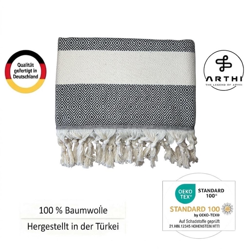 May include: A black and white patterned towel with a diamond design and white fringe. The towel has a white stripe in the middle. The text "100% Baumwolle" and "Hergestellt in der T&uuml;rkei" are visible.