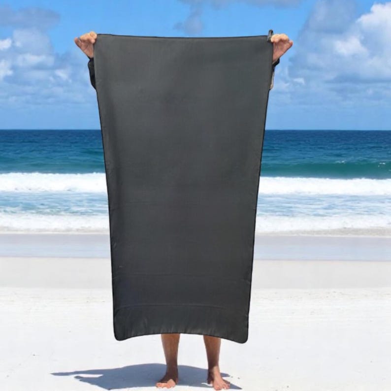 May include: A large, rectangular, solid black towel held upright. The towel features a smooth, uniform texture with a simple hemmed edge along the perimeter. The fabric appears opaque and matte, providing full coverage from the top to the bottom.