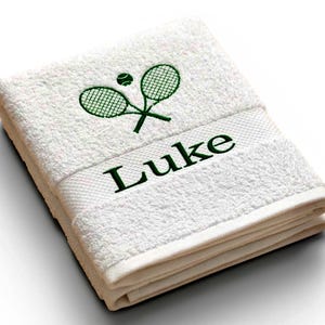 Puede incluir: Toalla blanca plegada con raquetas de tenis bordadas en verde, una pelota de tenis y el nombre "Luke". La toalla está hecha de un material suave y absorbente. Perfecta para deportistas y aficionados al tenis.