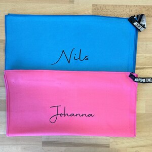 Pu&ograve; includere: Due asciugamani in microfibra, uno azzurro chiaro con il nome "Nils" scritto su di esso e uno rosa con il nome "Johanna" scritto su di esso.