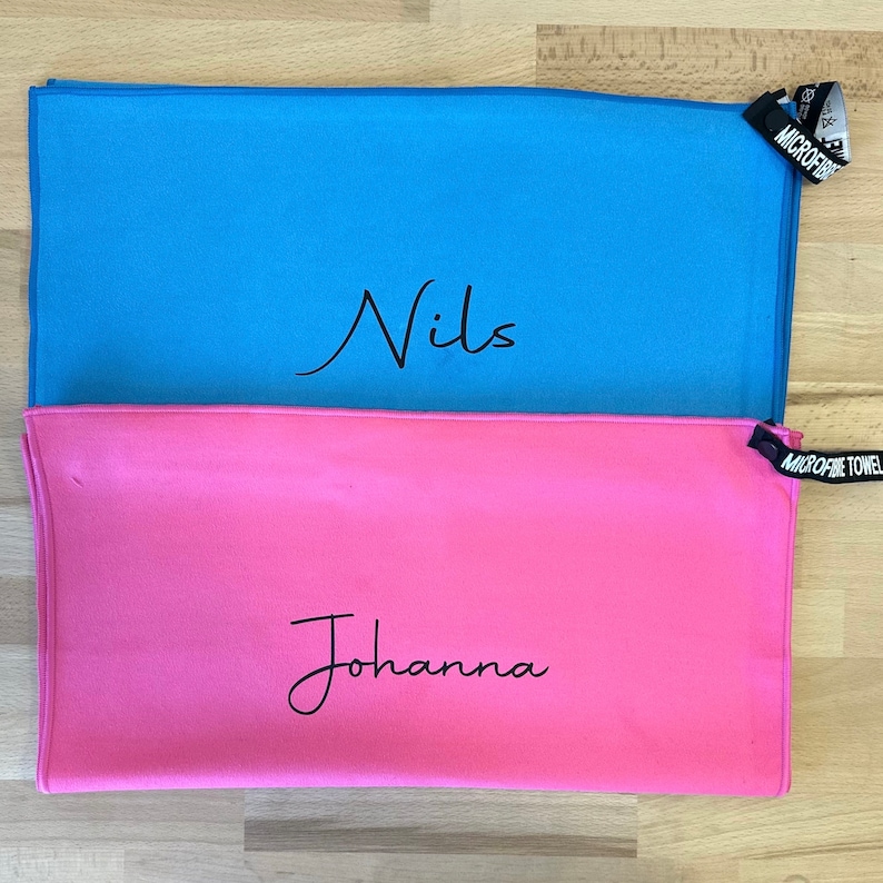 Pu&ograve; includere: Due asciugamani in microfibra, uno azzurro chiaro con il nome "Nils" scritto su di esso e uno rosa con il nome "Johanna" scritto su di esso.