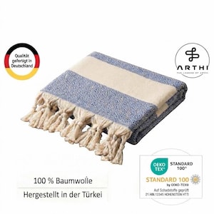 K&ouml;nnte beinhalten: Eine gefaltete blau-cremefarbene Decke mit geometrischem Rautenmuster und langen cremefarbenen Quasten an der Kante. Die Decke enth&auml;lt Textetiketten mit Angaben zu 100 % Baumwolle, t&uuml;rkischer Herkunft, deutscher Qualit&auml;t und Oeko-Tex Standard 100 Zertifizierung.