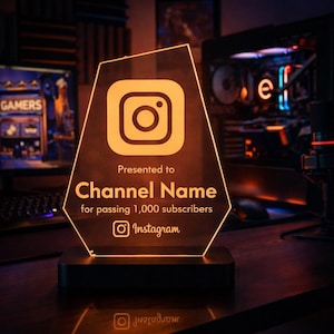 Puede incluir: Un premio de acrílico brillante con el logotipo de Instagram y el texto "Presented to Channel Name for passing 1,000 subscribers". El premio está sobre una base negra, ideal para un creador de contenido.