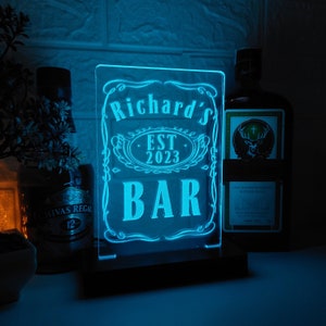 May include: A glowing blue LED bar sign with the name "Richard's" and "EST 2023" displayed. The word "BAR" is prominently featured at the bottom. The sign is mounted on a dark wooden base.