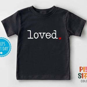 May include: Black short-sleeved t-shirt with the word "loved" in white text and a small red heart.