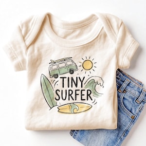 May include: A cream-colored short-sleeve bodysuit featuring a graphic print of a green van with a surfboard on top, a yellow sun, a green wave, and a yellow surfboard. The text "TINY SURFER" is printed in black letters in the center of the design.