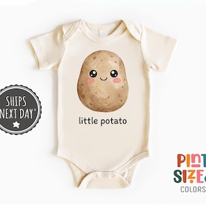 May include: Cream-colored baby bodysuit with a smiling potato graphic. The potato has a brown, textured appearance with black eyes and pink cheeks. The words "little potato" are printed below the graphic.