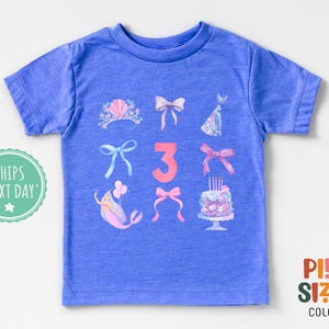 May include: A blue t-shirt with a pink number three and various pink and white illustrations of a mermaid, a crown, bows, and a birthday cake. The text "Ships Next Day" is in the top left corner.