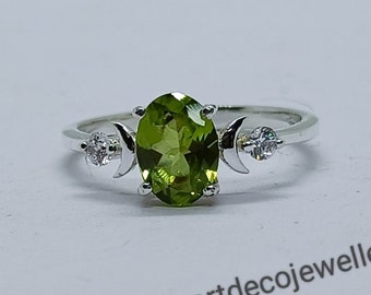 Puede incluir: Un anillo de plata con una piedra ovalada verde y dos piedras blancas más pequeñas engastadas en forma de media luna a cada lado.