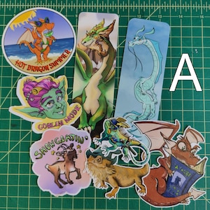 Könnte beinhalten: Eine Sammlung von Aufklebern und Lesezeichen mit verschiedenen Illustrationen, darunter ein orangefarbener Drache mit Sonnenbrille, ein grünes Koboldgesicht mit dem Text GOBLIN MODE, eine Ziege mit dem Text SHOW GOATIN, eine Bartagame und zwei lange Drachen-Lesezeichen.