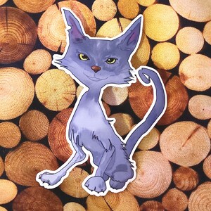 Könnte beinhalten: Ein Aufkleber mit einer stilisierten, hellvioletten Katze mit gelben Augen und einem gebogenen Schwanz. Die Katze sitzt mit einer ausgestreckten Pfote. Der Hintergrund ist ein Muster aus braunen und gelben Holzscheiben.