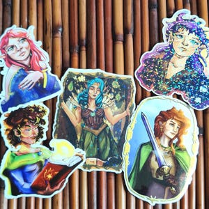 Könnte beinhalten: Eine Sammlung von Fantasy-Stickern mit Illustrationen von Elfen mit verschiedenen Haarfarben und -kleidung. Die Sticker zeigen Elfen mit roten, blauen und lila Haaren, und einer hält ein Schwert. Auf Bambushintergrund.