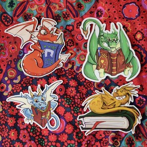 May include: Four colorful dragon stickers with different poses and expressions. Each dragon is holding or sitting on a book. The books have different covers and titles. The stickers are on a red and green patterned background.