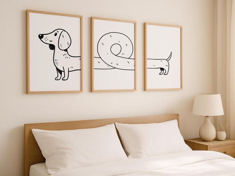 May include: Three framed art prints with a minimalist dachshund design. The prints, in light wood frames, show the dog in various poses, using black line art on a white background. The artwork is displayed above a bed, adding a touch of modern art.
