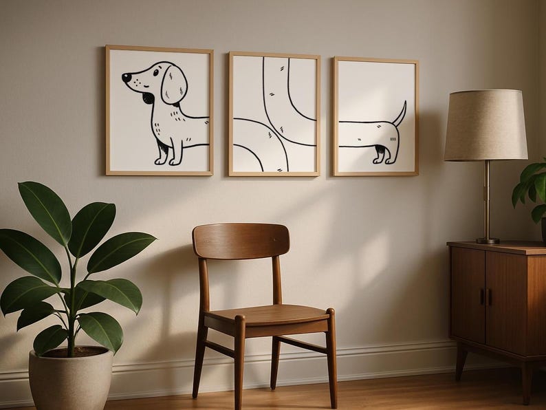 May include: Three framed art prints with black and white dachshund illustrations. The prints are in light wood frames, displayed on a neutral wall. A wooden chair and a potted plant are in the foreground, with a lamp and cabinet in the background.
