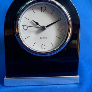 May include: A black and silver analogue clock with a white face and black hands. The clock is on a black base with a silver trim.