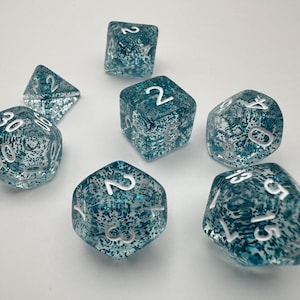 Puede incluir: Conjunto de dados azul turquesa con números blancos. Los dados son translúcidos y tienen un acabado brillante.