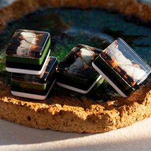 May include: Four rectangular tiles featuring a glossy black surface with white and copper-colored veining. Each tile has a layered design with a green middle band and a solid white base, arranged in a cluster with two stacked and two positioned flat.
