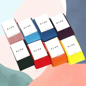 以下が含まれることがあります： 「KLUE」と白く書かれたラベルがついた、異なる色のソックスが8足。ソックスは虹色のパターンで並べられており、ピンク、ブルー、ターコイズ、パープル、グリーン、レッド、オレンジ、イエローの色が使われています。