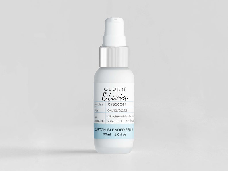 Puede incluir: Una botella blanca con una tapa de bomba plateada y una etiqueta que dice "OLURA Olivia" y "CUSTOM BLENDED SERUM 30ml - 1.0 fl oz".