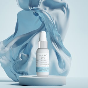 Puede incluir: Un frasco blanco de suero personalizado Olur'a you con un tap&oacute;n de bomba plateado. El frasco est&aacute; sobre un pedestal azul claro sobre un fondo azul claro.