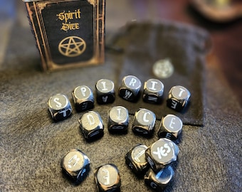 May include: Black spirit dice with white letters spelling out "Spirit Dice" on a dark brown surface. The dice are next to a small black book with gold trim and the words "Spirit Dice" on the cover.