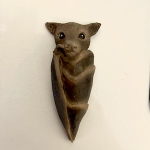 May include: A brown bat figurine with large ears and eyes, curled up in a sleeping position.
