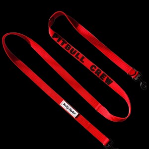 May include: Bright red dog leash with the text "PITBULL CREW" in black. The leash has a black metal clip and a small white tag that says "Bully Styler". The leash is made of a durable, woven material.