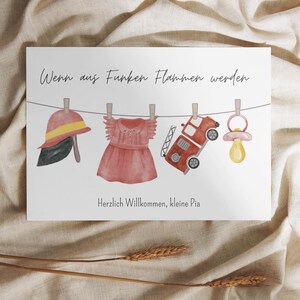 Könnte beinhalten: Aquarell-Illustration mit Baby-Artikeln, die an einer Wäscheleine hängen. Enthält einen Feuerwehrhelm, ein Kleid, ein Feuerwehrauto und einen Schnuller. Der Text lautet: "Wenn aus Funken Flammen werden" und "Herzlich Willkommen, kleine Pia."