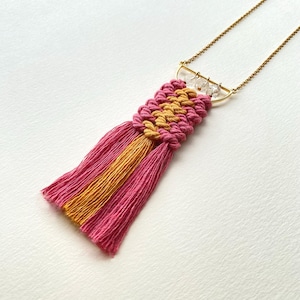 Può includere: Una collana con nappe in macramè rosa e oro con un ciondolo a forma di mezzaluna dorata e perline di cristallo trasparenti.