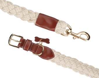 May include: A white braided rope dog leash with brown leather accents and a gold metal clasp. The leash is attached to a matching white braided rope dog collar with a brown leather buckle and a gold metal bone charm.