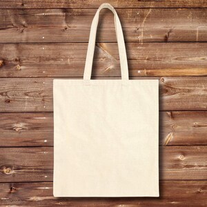 Back view of natural cotton canvas tote bag shown against a warm wooden plank wall background. The bag is blank with no print, featuring long reinforced shoulder straps and a structured flat-bottom shape.