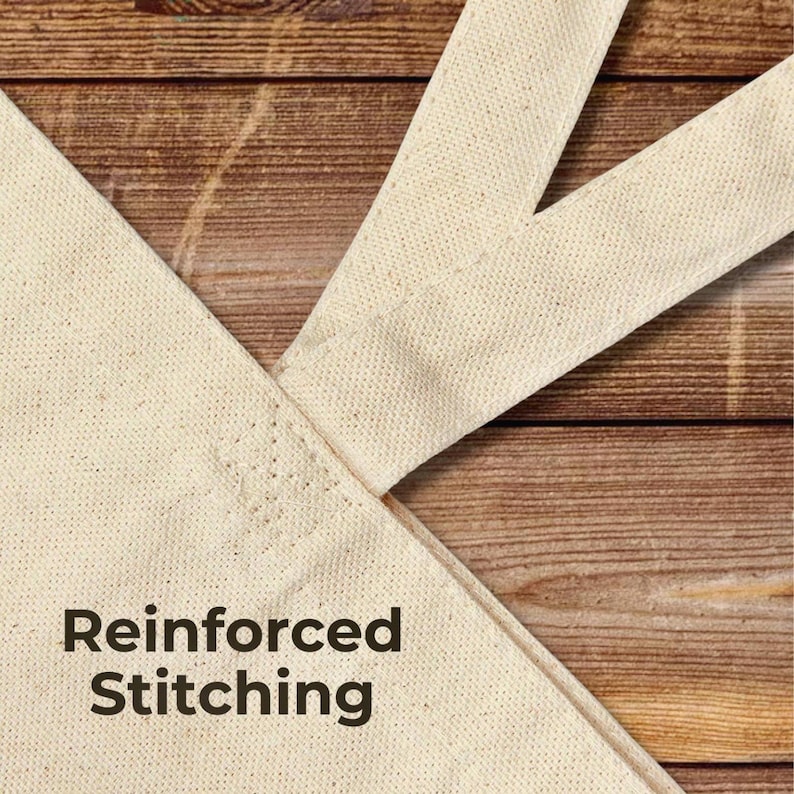 Close-up detail of a natural cotton canvas tote bag handle showing reinforced stitching at the seam. The fabric texture and stitching are clearly visible, highlighting durability and quality construction. The tote is photographed on a turquoise painted wooden background with the text “Reinforced Stitching” displayed in the lower corner.