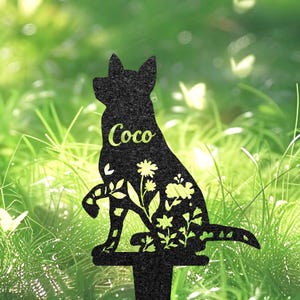 May include: Black metal dog silhouette garden stake with floral cutouts. The dog's name, "Coco", is written in a light green font. The stake is designed for gardens, adding a decorative touch to outdoor spaces.