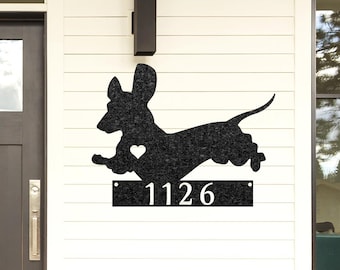 May include: Black metal dachshund silhouette with a heart cutout and a white number plaque with the number 1126. The house number plaque is attached to the dachshund silhouette.