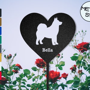 Puede incluir: Estaca de jard&iacute;n de metal negro en forma de coraz&oacute;n con una silueta blanca de un perro dentro del coraz&oacute;n. La estaca tiene el nombre "Bella" escrito debajo del perro. La estaca est&aacute; delante de un arbusto de rosas rojas.