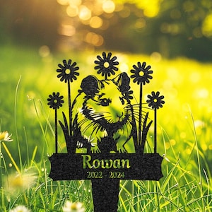 May include: Black metal garden memorial with a silhouette of a hamster surrounded by flowers. The memorial has the name "Rowan" and the dates "2022 - 2024" engraved on it.