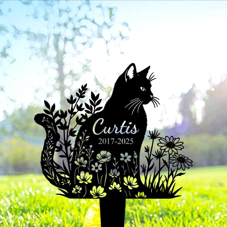 May include: A black metal garden stake featuring a silhouette of a cat surrounded by floral patterns. The name Curtis and the years 2017-2025 are engraved in white script and sans-serif font on the body of the cat, which is perched on a stake.